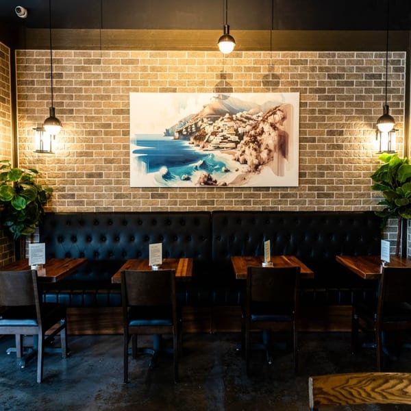 Bellissima Italian Mediterranean Restaurant interior with brick walls, black booths, wooden tables, and a large coastal painting.