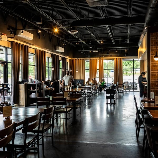 Spacious Bellissima Italian Mediterranean Restaurant dining room with dark tables, chairs, and exposed ceiling, with patrons.