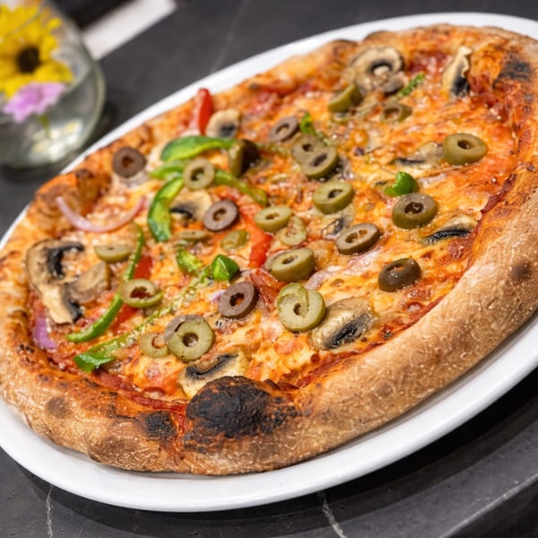 A freshly baked pizza with mushrooms, green peppers, red onions, and olives on a white plate.